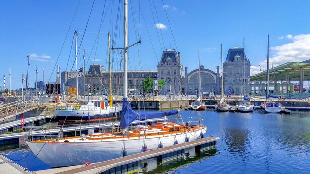 A marina with boats docked, a large building with a clock tower, and a covered area with bicycles. - Cozy apartment in Oostende with WiFi (Oostende)
