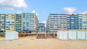 A beachfront hotel with multiple floors, a sandy beach in the foreground, and a clear sky. - Cozy apartment in Oostende with WiFi (Oostende)