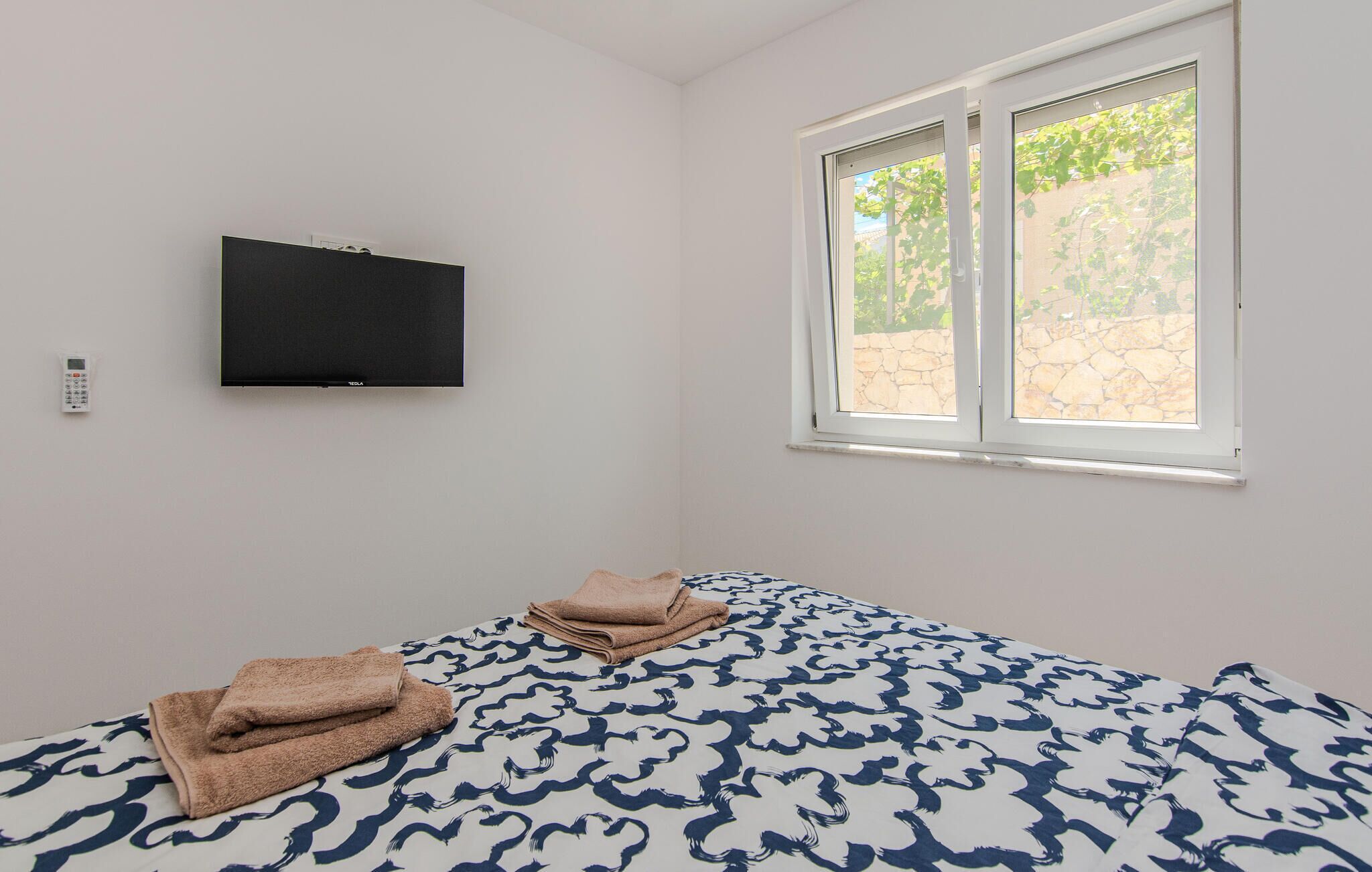 Quarto com cama, televisão na parede e janela com vista para o verde.
