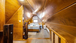 Een gezellige slaapkamer onder een schuin houten dak, met een bed met witte dekbedovertrek, nachtkastje en een raam dat natuurlijk licht binnenlaat.
