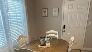 Un comedor con una mesa redonda de madera, cuatro sillas, dos lámparas fijadas a la pared y dos cuadros enmarcados.