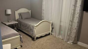 A bedroom with a bed, a nightstand, a lamp, a ceiling fan, and a window with curtains.