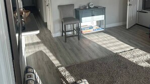 Un salón amplio con un televisor de pantalla plana grande montado en la pared, un sillón gris, un mueble pequeño azul y una alfombra estampada.