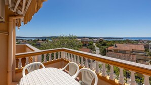 Un balcon avec une table et des chaises, donnant sur une ville côtière avec ses maisons et une étendue d’eau.