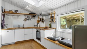 Une cuisine de taille réduite, dotée de plans de travail en bois, d’armoires blanches et d’un puits de lumière.