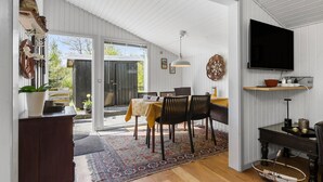 Un coin repas avec une table dressée pour quatre personnes, un téléviseur fixé au mur et une grande fenêtre donnant sur l’extérieur.