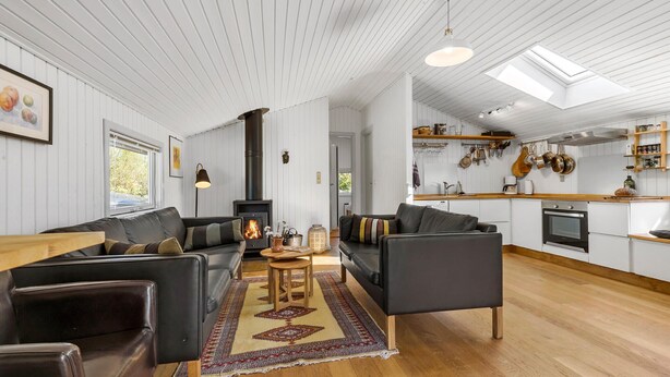Un salon moderne avec une cheminée, une cuisine dotée d’étagères en bois et un coin repas.
