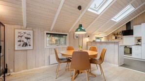 A wooden interior with a round dining table, chairs, a green pendant light, and a kitchen area with cabinets and appliances. - Gorgeous home in Oksbøl with sauna (Oksbøl)