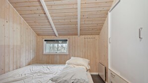 A bedroom with a wooden ceiling, a window with a view of trees, a bed with white bedding, and a white wardrobe with drawers. - Gorgeous home in Oksbøl with sauna (Oksbøl)