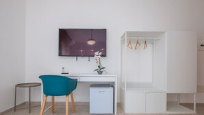 Ein modernes Zimmer mit Schreibtisch, Stuhl, Fernseher und einem weißen Kleiderschrank.