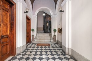 Un pasillo con piso a cuadros, puertas de madera y una escalera que sube a un nivel superior.