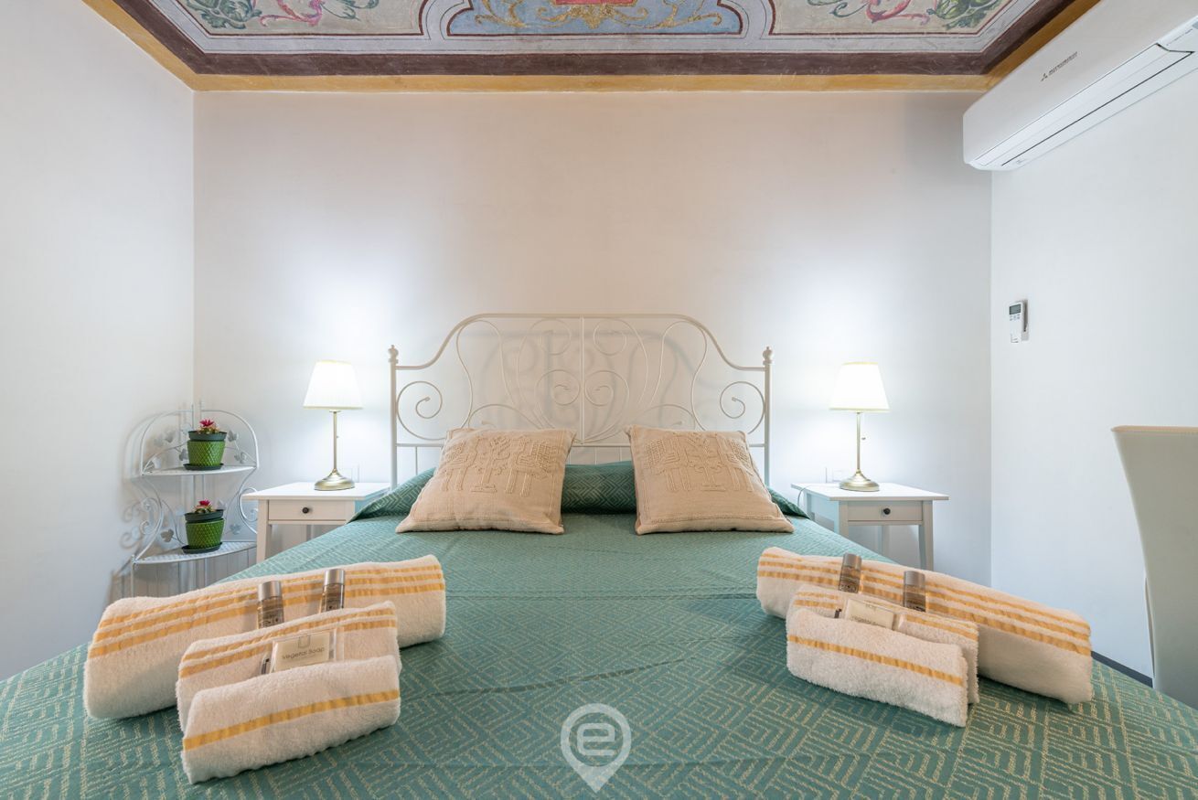 Ein Hotelzimmer mit einem Bett, zwei Nachttischen, Lampen, einer dekorativen Decke und einer Wand-Klimaanlage.