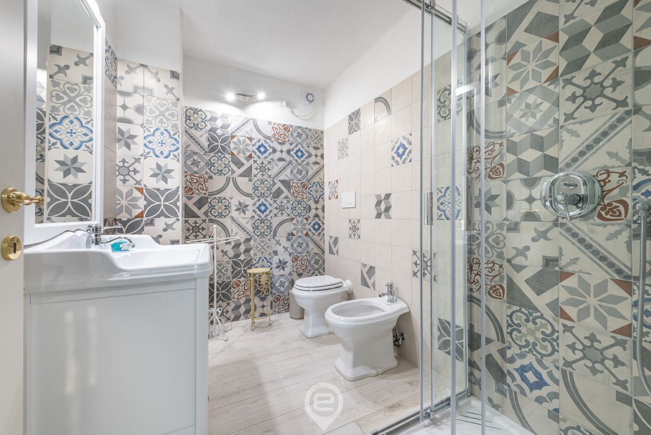 Ein Badezimmer mit einem weißen Waschbecken, zwei Toiletten, einem Bidet und einer Duschkabine aus Glas.