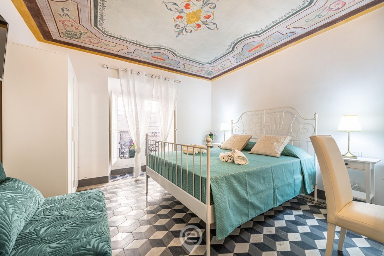 Ein Schlafzimmer mit einem Bett, einem Sessel, einem Nachttisch und einer Zierteilung an der Decke.
