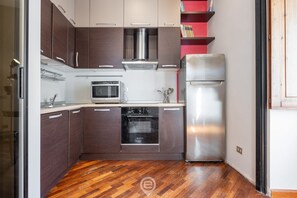 A compact kitchen with dark brown cabinets, a stainless steel range hood, a microwave, an oven, and a refrigerator. - Charm in Via Abba - Cagliari (Cagliari)