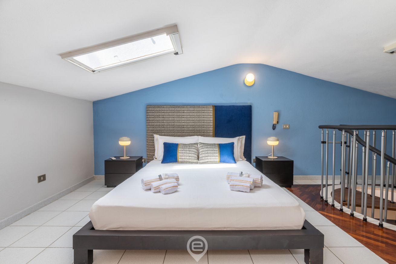 Une chambre à coucher avec un grand lit, deux tables de chevet avec des lampes, une tête de lit et un escalier.