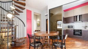 Une cuisine moderne avec un coin repas, comprenant un escalier en colimaçon, une table ronde avec des chaises et un mur d’accent rouge.