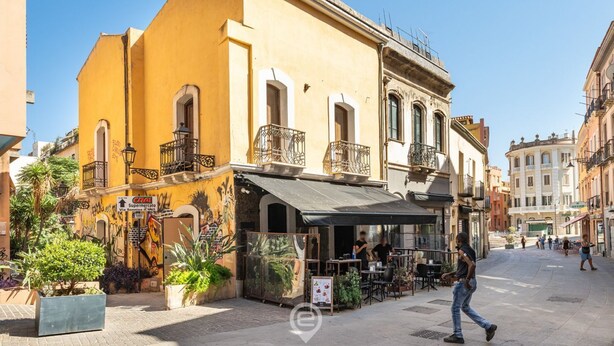 Une rue avec un immeuble jaune doté d’une terrasse et d’une enseigne indiquant un supermarché.