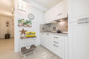 A modern kitchen with white cabinets, a clock, potted plants, and a star decoration.