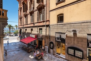 A street view with outdoor seating at a café, a shop with a black awning, and a building with a stone facade.
