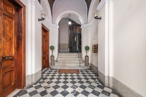 A hallway with a checkered floor, wooden doors, and a staircase leading to another room.