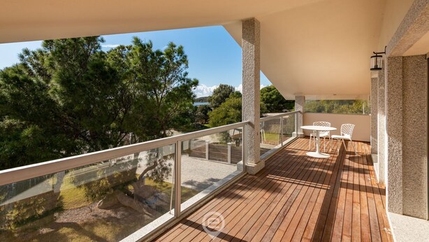 Une terrasse en bois avec des rampes en verre, des meubles d’extérieur et une vue sur des arbres et une étendue d’eau.