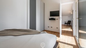 Une chambre moderne avec un lit, un téléviseur à écran plat fixé au mur et une porte-fenêtre coulissante donnant sur un balcon.