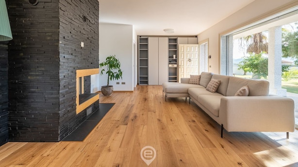 Un salon moderne avec un plancher en bois, un canapé beige, un mur en briques noires et une grande fenêtre.