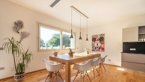 Une cuisine moderne avec une table en bois, des chaises blanches, des luminaires suspendus et une grande fenêtre.