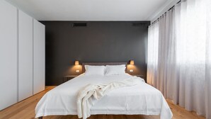 Une chambre moderne avec un grand lit, deux lampes de chevet et un mur d’accent de couleur foncée.