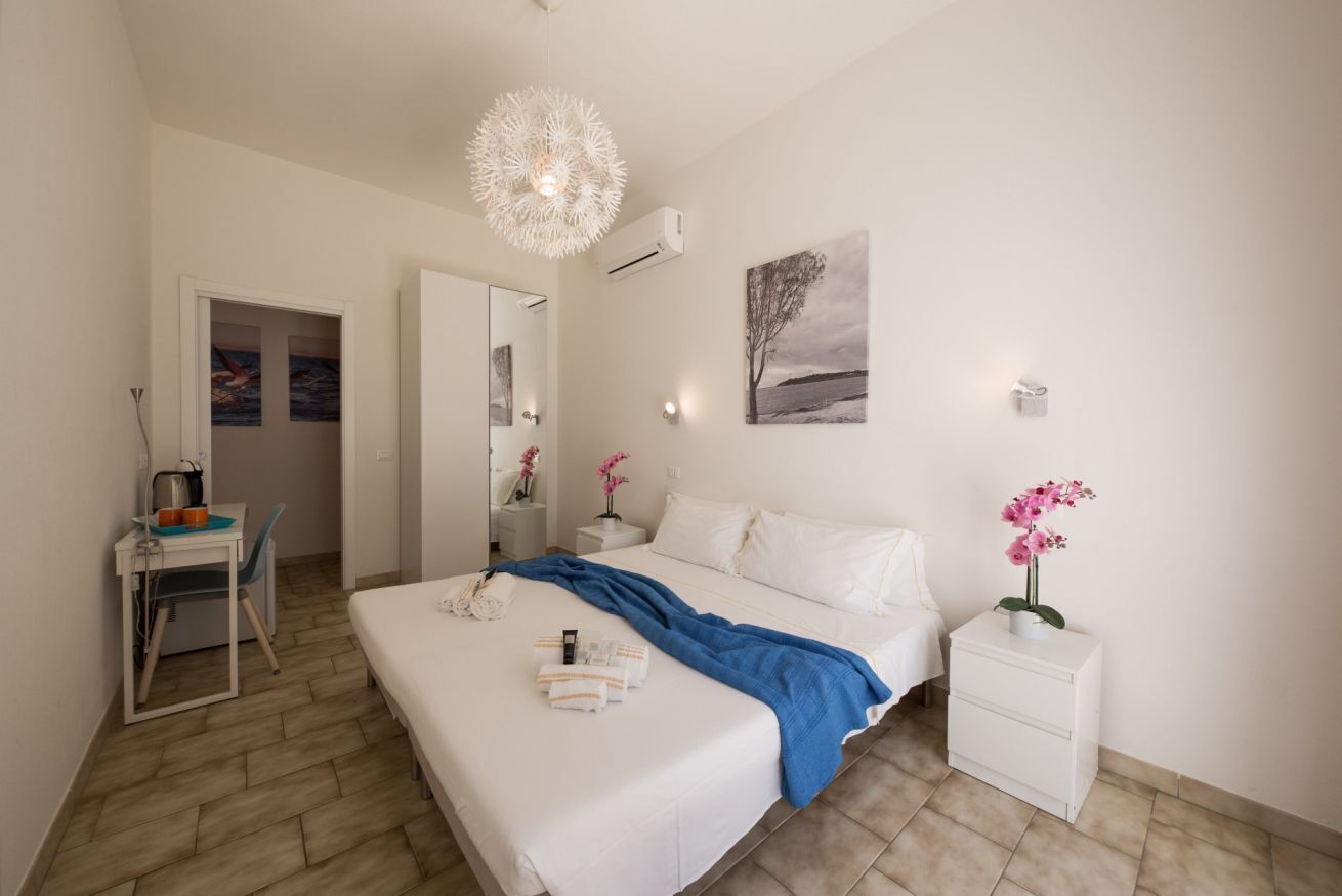 Una habitación de hotel moderna con una cama grande, un escritorio con una silla, una mesita de noche con lámpara y un aire acondicionado instalado en la pared.