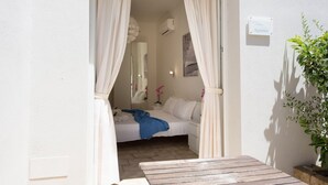 A bedroom with a bed, curtains, a bedside table, and a small potted plant. - Coru e Mari - Suite Nora (Pula)