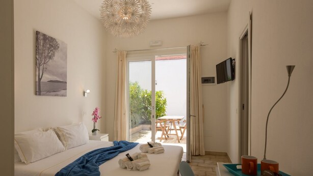 A hotel room with a bed, a desk, a chair, a TV, and a balcony with a table and chairs. - Coru e Mari - Suite Nora (Pula)