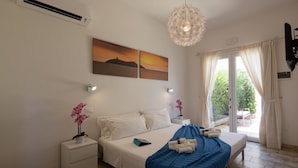 A hotel room with a bed, bedside tables, a nightstand, a decorative hanging light, a painting, and a view through the window. - Coru e Mari - Suite San Macario (Pula)