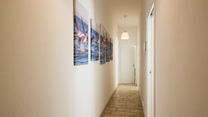 A hallway with a tiled floor, white walls, and a series of framed artworks on the left. - Coru e Mari - Suite San Macario (Pula)