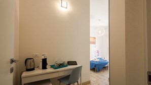 A hotel room with a desk, chair, and a bed with a blue bedspread. - Coru e Mari - Suite San Macario (Pula)