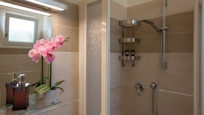 A modern bathroom with a glass shower enclosure, a potted orchid, and a mirror with a light above it. - Coru e Mari - Suite San Macario (Pula)