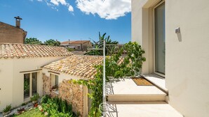 A courtyard with a stone building, a tiled roof, and a modern white building with a large window and a door. - Il Ginepro - Suite Mare (Pula)
