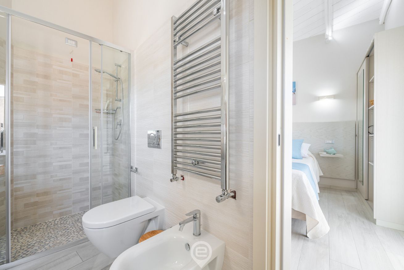 Un baño moderno con cabina de ducha de vidrio, inodoro blanco y lavamanos empotrado.