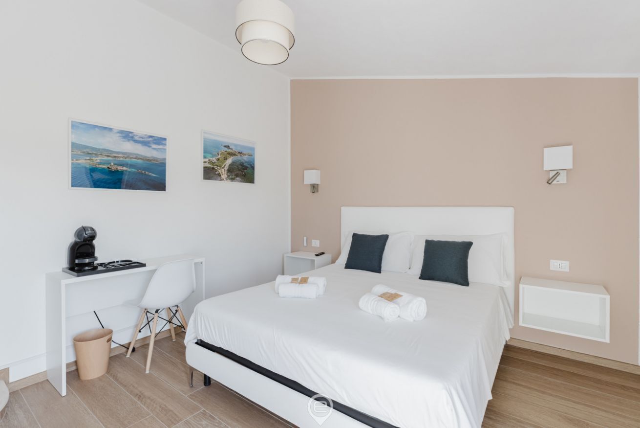 Moderni hotellihuone, jossa on suuri sänky, työpöytä ja kaksi seinälle ripustettua taulua.
