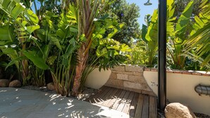 Un jardín con una terraza de madera, un muro de piedra y exuberante vegetación tropical.