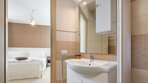 Una habitación de hotel moderna con una cama grande, un lavamanos blanco y un espejo encima.