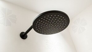 A black showerhead mounted on a white wall with a leaf pattern. - KyS Castello - Suite Marina (Cagliari)