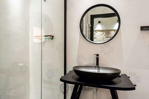 A bathroom with a modern design, featuring a round mirror, a black sink on a black pedestal, and a frosted glass door.