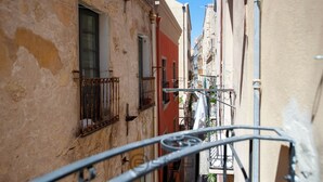 A narrow street with buildings on either side, featuring balconies and a metal railing in the foreground. - KyS Castello - Suite Marina (Cagliari)