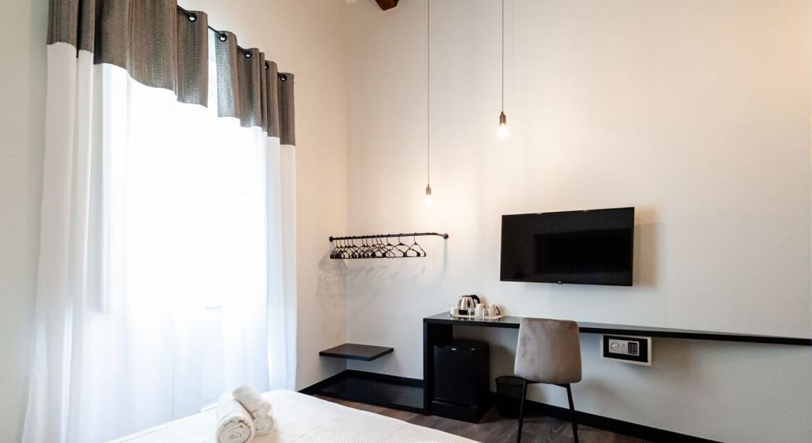 Une chambre d’hôtel moderne équipée d’un lit, d’un bureau avec une chaise, d’un téléviseur fixé au mur et d’une petite étagère avec une bouilloire.