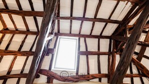 A rustic ceiling with exposed wooden beams and a skylight.
