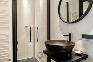 A modern bathroom with a large, dark-colored vessel sink, a round mirror, and a glass shower enclosure with a frosted pattern. - KyS Castello - Suite Stampace (Cagliari)