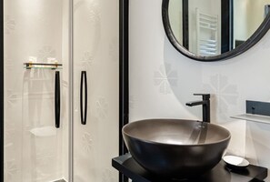 Ett modernt badrum med en stor, svart tvättställsskål, en rund spegel och dörrar av frostat glas.