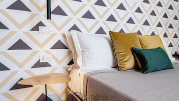 Una camera d'albergo ordinata con carta da parati decorata, un letto con cuscini, un comodino e una lampada.